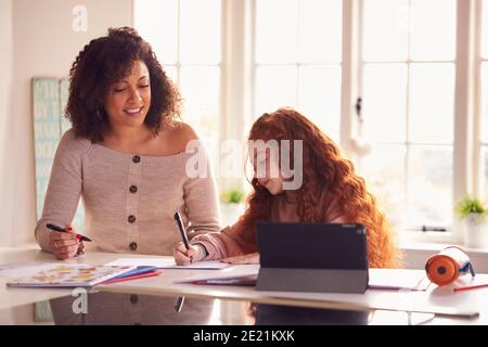 Mother Helping Daughter With Homework Sitting At Kitchen Counter Using Digital Tablet Together Stock Photo