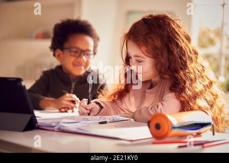 Two Children Sitting At Kitchen Counter Doing Homework Using Digital Tablet Stock Photo
