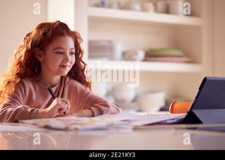 Girl Sitting At Kitchen Counter Doing Homework Using Digital Tablet Stock Photo