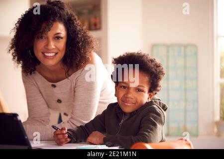 Portrait Of Mother Helping Son With Homework Sitting At Kitchen Counter Using Digital Tablet Stock Photo