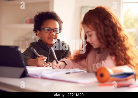 Two Children Sitting At Kitchen Counter Doing Homework Using Digital Tablet Stock Photo