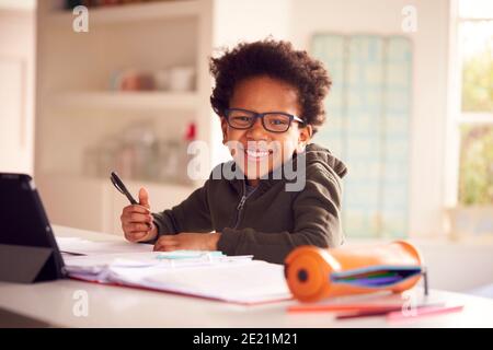 Portrait Of Boy Sitting At Kitchen Counter Doing Homework Using Digital Tablet Stock Photo