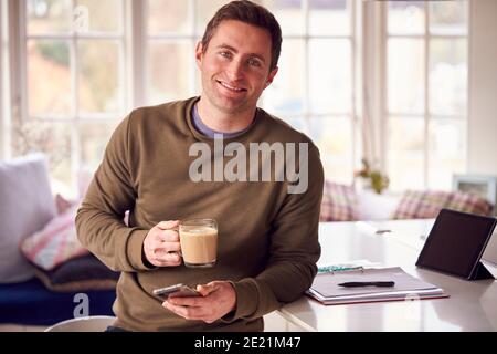 Portrait Of Man With Digital Tablet Working From Home On Kitchen Counter Drinking Coffee Stock Photo