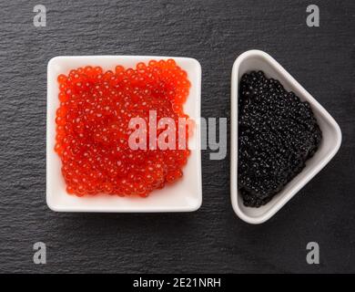grainy caviar of paddlefish fish in a white ceramic plate and red chum salmon caviar in a white ceramic bowl, black background, top view Stock Photo