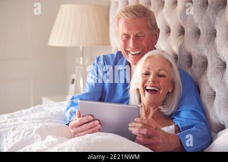 Senior Couple At Home In Bed Self Isolating Using Digital Tablet During Covid 19 Lockdown Stock Photo