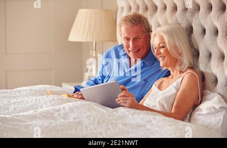 Senior Couple At Home In Bed Self Isolating Using Digital Tablet During Covid 19 Lockdown Stock Photo