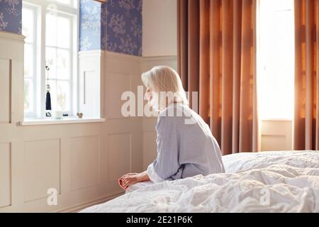 Unhappy And Depressed Senior Woman Sitting On Edge Of Bed At Home Stock Photo