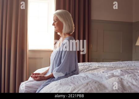 Senior Woman Sitting On Edge Of Bed At Home Meditating During Lockdown For Covid-19 Stock Photo