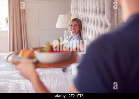 Man Bringing Woman Breakfast In Bed To Celebrate Wedding Anniversary Stock Photo