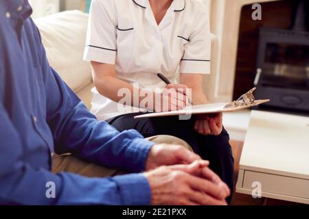 Close Up Of Female Doctor Making Notes During Home Visit To Senior Man For Medical Check Stock Photo