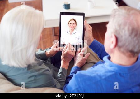 Female Doctor Having Video Consultation With Senior Couple On Digital Tablet At Home Stock Photo