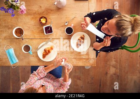 Two Female Friends Meet In Coffee Shop Putting On Mask And Using Hand Sanitizer In Health Pandemic Stock Photo