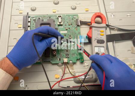 Volgograd, Russia - September, 2020: Diagnostics of printed circuit board TV. Hands hold the resistance test lead. Selective focus. Stock Photo