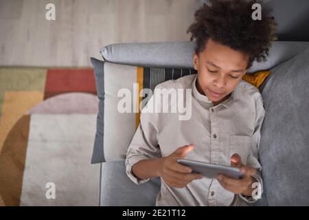 From above view medium portrait of teen boy relaxing on sofa at home playing video game on smartphone, copy space Stock Photo