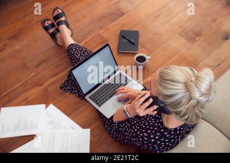 Overhead View Of Businesswoman On Phone On Floor With Laptop Working From Home In Pandemic Lockdown Stock Photo