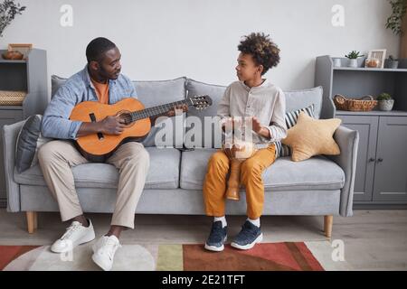 Horizontal full shot of African American man and his son spending time together at home playing guitar and djembe Stock Photo
