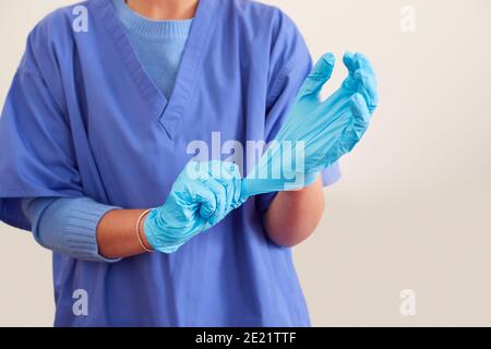 Close Up Of Female Nurse Wearing Scrubs Putting On Sterile PPE Gloves Stock Photo