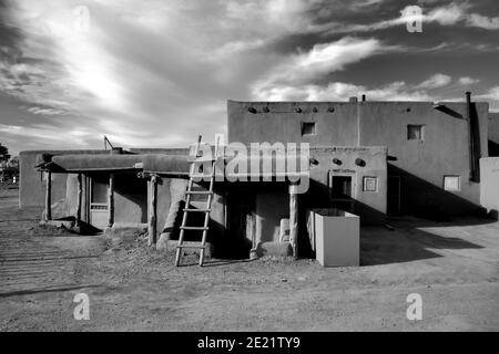 Grayscale shot of old houses under the sunlight and a cloudy sky in Taos Pueblo, New Mexico Stock Photo