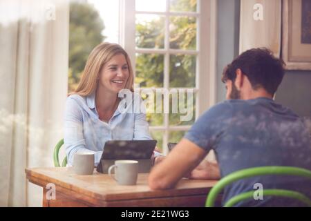 Couple With Digital Tablet Sitting At Table Working From Home Viewd Through Window Stock Photo