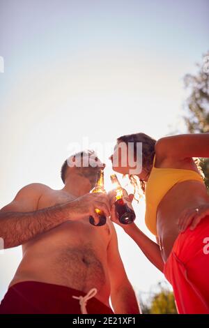 Couple Wearing Swimming Costumes Standing In Paddling Pool In Summer Garden At Home Drinking Beer Stock Photo