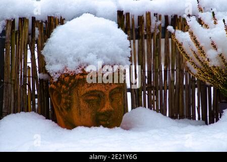 Old weathered terracotta buddha head covered with snow Stock Photo