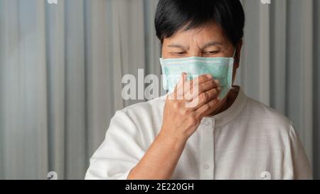 asian old woman wearing a face mask indoor coughing Stock Photo