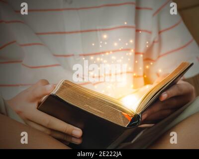 Hand of child opening the gold edge magic book with mystic bright spark light on dark background. Fantasy and discovery magic concept. Stock Photo