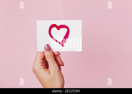 Woman's hand holding a paper card with heart symbol drawn on it Stock Photo