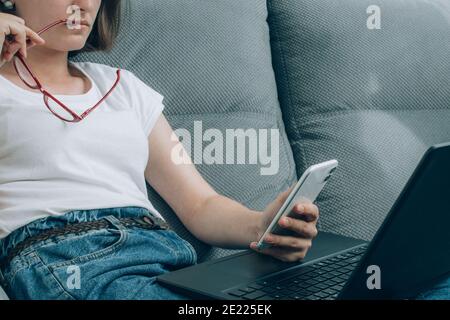 Young woman checking phone - using both laptop and smartphone. Social network, online safety and digital lockdown in USA concept. Internet censorship Stock Photo