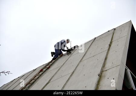 The roof roofer climbs up the ladder to the roof of the house to fix sheet metal roof Stock Photo