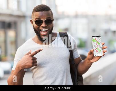 Gps App. Cheerful Black Man Pointing At Smartphone With Opened Navigation Maps Stock Photo