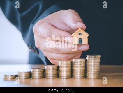 Businessman's hand placing house on coins is saving money of coins to buy a home concept for property ladder, real estate investment and mortgage for Stock Photo