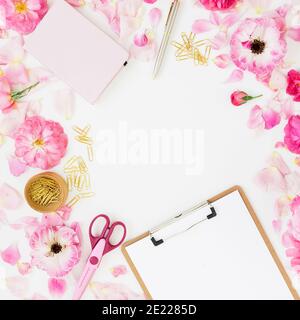 Stylish frame workspace with clipboard, notebook, pink flowers and accessories on white background. Flat lay, top view. Stock Photo
