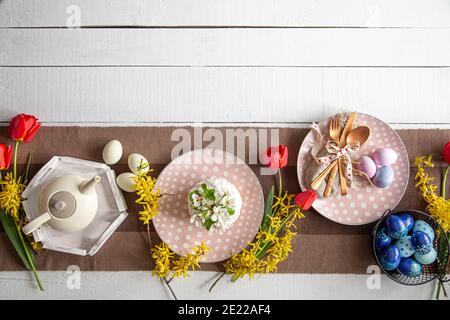 Festive cake, teapot, eggs and flowers on the table. Easter celebration and table setting concept. Stock Photo