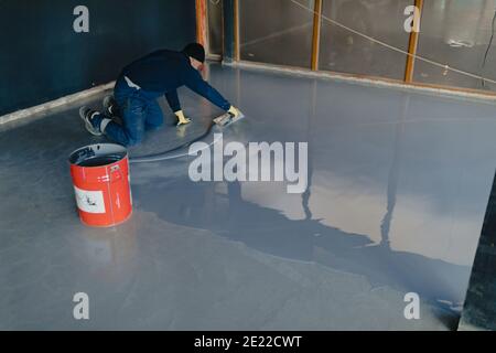 The worker applies gray epoxy resin to the new floor Stock Photo