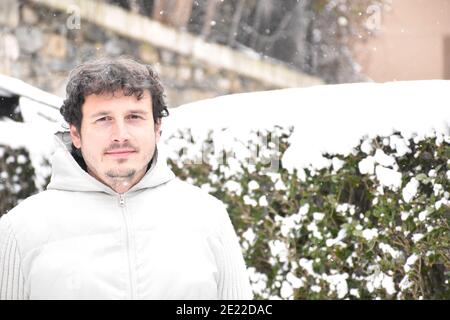 Portrait of man smiling and mysterious look next to snowy bushes. Dressed in a white jacket, brown hair with gray hair. Snow day in Munilla, La Rioja. Stock Photo