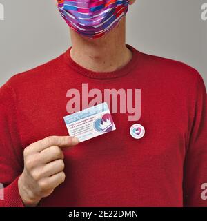 Vaccinated man wearing face mask and holding NHS Covid 19 vaccination record card