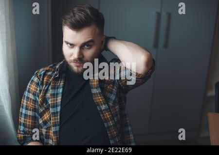 Bearded caucasian man is touching his head posing pensive at home looking at camera Stock Photo