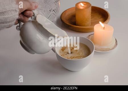 Feminine hand pouring milk from vintage style milk jug into cup of coffee Stock Photo