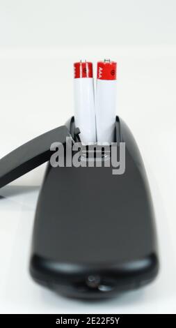 Black TV remote control with AAA alkaline batteries on a white background. Battery replacement, spare parts. Close up of the battery compartment of th Stock Photo