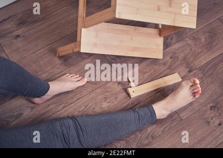 Young woman fell down stairs due to broken wooden stepladder leg and injured foot. The problem with labor protection at diy work at home Stock Photo