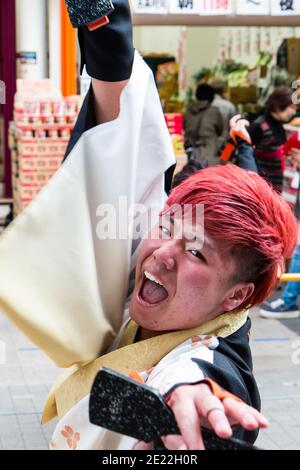 Hinokuni Yosakoi dance festival with close up of face of Japanese male dancer, eye-contact with viewer, mouth open, singing, holds naruko. Motion blur Stock Photo