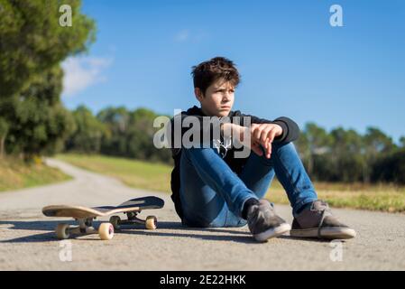 Handsome teen male with a skateboard sitting on asphalt road Stock Photo