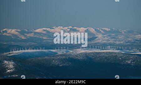 Windmills against snowcapped mountain peaks on a clear blue skies day, Sierra de Guadarrama, Madrid Stock Photo