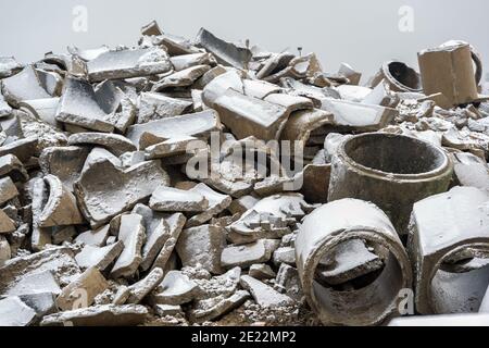 Heap of broken concrete drainage pipes under a thin layer of snow on a construction site, waiting for debris disposal, selected focus Stock Photo