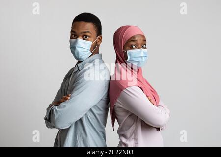 Surprised muslim couple in masks standing back to back Stock Photo