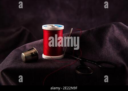 Thread, needle, thimble, and scissors against a dark background. Stock Photo