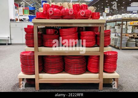 Plates and cups are sold at the store. Rows of different red kitchen utensils for home on shelves in a mall. Stock Photo