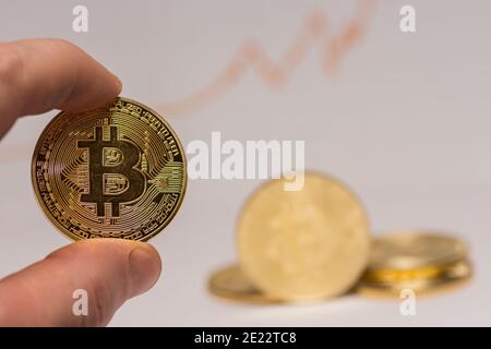 valuable bitcoin held between two fingers with other coins in the background Stock Photo