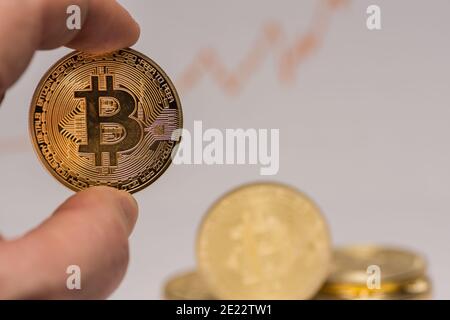 bitcoin held between two fingers with other coins in the background detail view Stock Photo